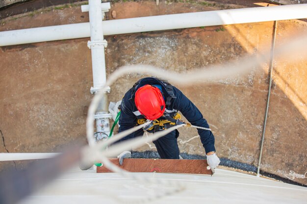 Bovenaanzicht foto van industriële lasser met touwtoegang die op hoogte werkt met een harnas, helm veiligheidsuitrusting touwtoegangsinspectie van de industrie van de dikteopslagtank.