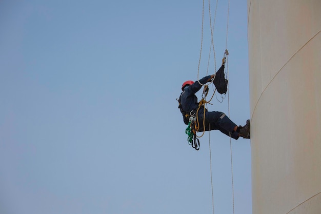 Bovenaanzicht foto van industriële lasser met touwtoegang die op hoogte werkt met harnashelm veiligheidsuitrusting touwtoegangsinspectie van dikte opslagtank