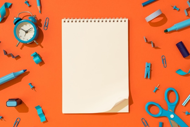 Bovenaanzicht foto van open spiraal notebook met gekrulde hoek en schoolbenodigdheden blauw briefpapier op geïsoleerde oranje achtergrond met lege ruimte