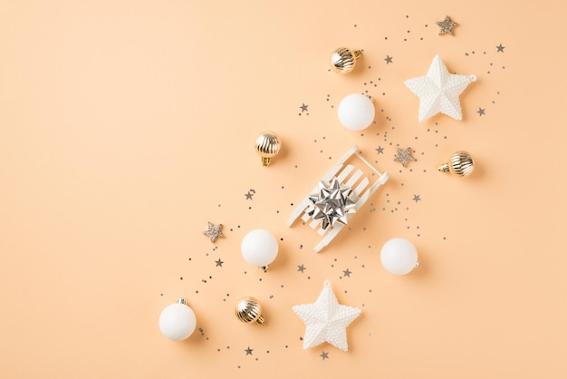 Bovenaanzicht foto van rij samenstelling witte en gouden kerstboom decoraties kleine slee met zilveren ster ballen sterren en pailletten op geïsoleerde beige achtergrond met copyspace