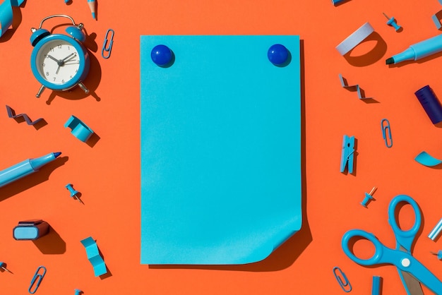 Bovenaanzicht foto van ronde met plastic bedekte magneten op levendig blauw vel papier met gekrulde hoek en schoolaccessoires blauwe briefpapier op geïsoleerde oranje achtergrond met lege ruimte