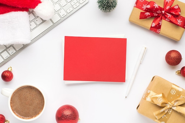 Bovenaanzicht foto van toetsenbord kopje warm drinken kerstman hoed grenen speelgoed rode kerstboom ballen geschenkdozen rode kaart en pen op geïsoleerde witte achtergrond met lege ruimte