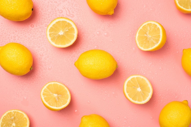 Bovenaanzicht foto van waterdruppels gesneden en hele gele citroenen op geïsoleerde pastelroze achtergrond