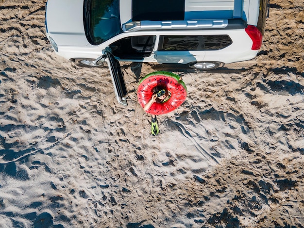 Bovenaanzicht gelukkige vrouw die uit de auto stapt in flippers met opblaasbare ring en tas kopieerruimte