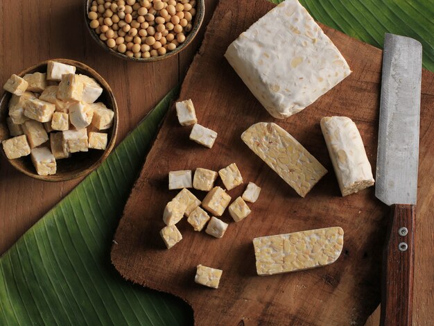 Bovenaanzicht gesneden rauwe tempeh snijden op houten snijplank boven rustieke bruine tafel met bananenblad