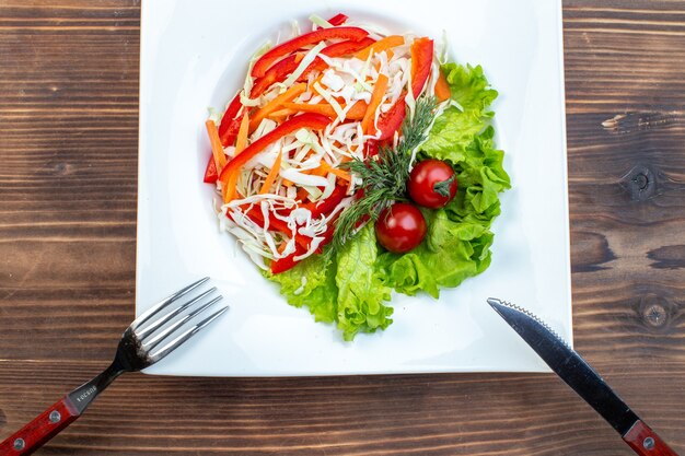 Bovenaanzicht groentesalade met groene salade en kool in plaat op bruin oppervlak