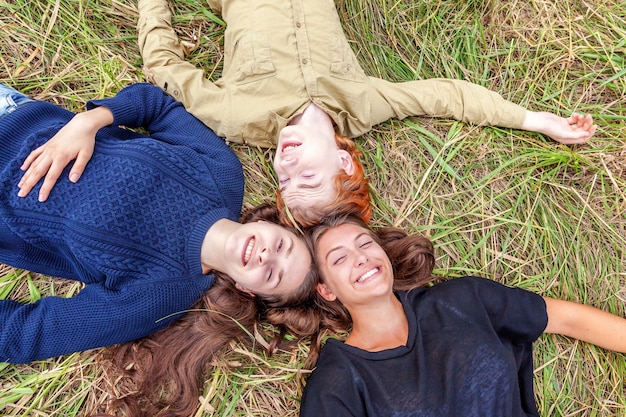 Bovenaanzicht groep van drie vrienden liggend op gras in cirkel glimlachen