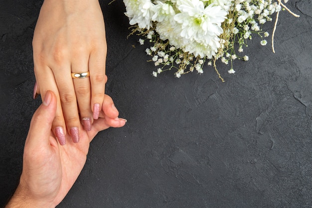 Bovenaanzicht handen bereiken mannelijke hand met vrouwelijke hand met verlovingsring bloemen op donkere achtergrond vrije ruimte