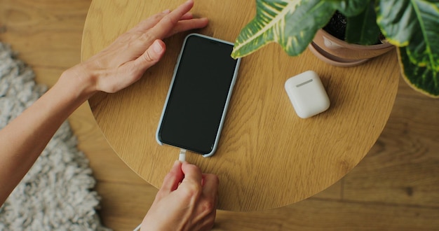 Bovenaanzicht Handen van vrouw die oplaadkabel in mobiele telefoon aansluit