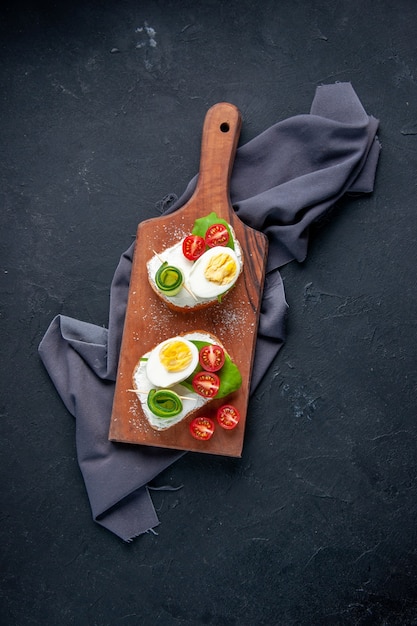 bovenaanzicht heerlijke sandwiches met tomaten komkommers en eieren op snijplank donkere achtergrond maaltijd hamburger eten ontbijt lunch snack sandwich toast