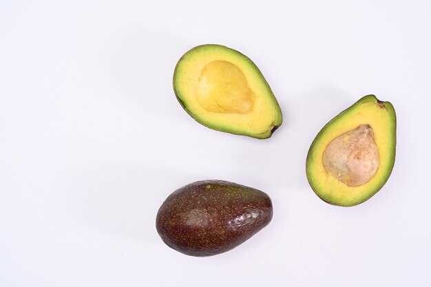 Bovenaanzicht hele en halve avocado met zaad op witte achtergrond.