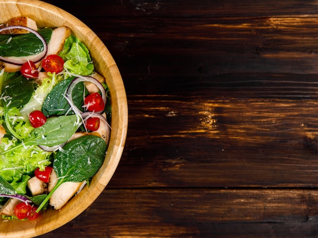 Bovenaanzicht hoek foto van gegrilde kipfilet verse en filet groentesalade met een verscheidenheid aan soorten natuurlijke groenten in houten kom op hout achtergrond. Gezond en dieet menu idee.