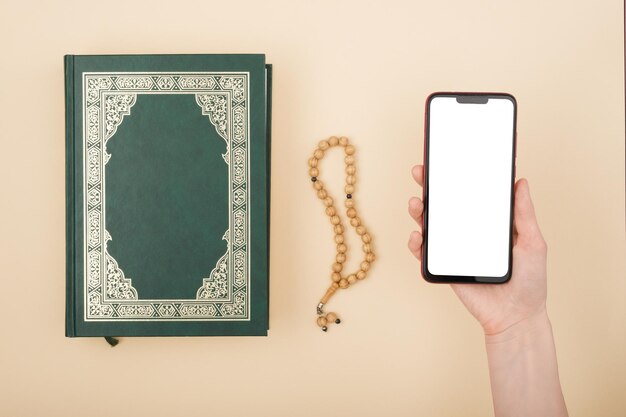 Bovenaanzicht Holly boek Koran rozenkrans smartphone in de hand op een beige achtergrond mock up