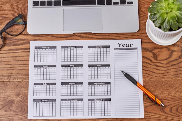 Bovenaanzicht jaarkalender met pen en plant op houten bureau plat leggen zakelijke kalender en andere toegang