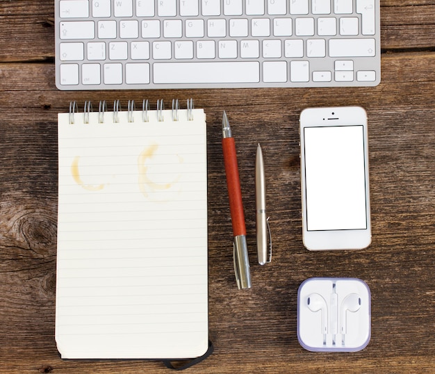 Bovenaanzicht kantoorwerkplek. toetsenbord met telefoon en lege notebook op houten tafel