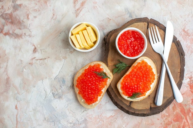 Bovenaanzicht kaviaar sandwiches met bestek en kaas op snijplank op lichte ondergrond