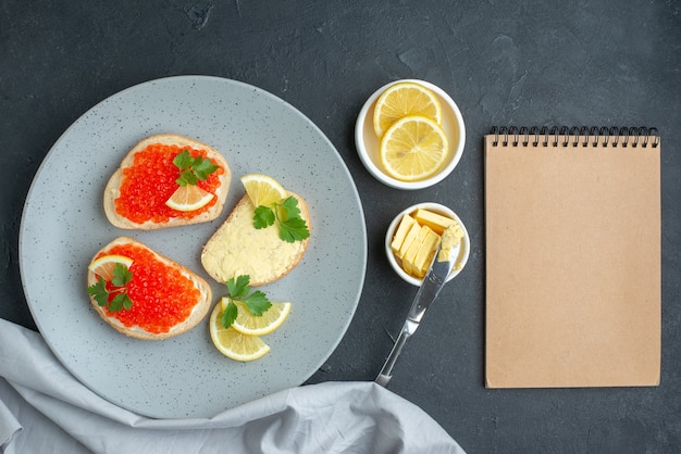 bovenaanzicht kaviaar sandwiches met citroen en bestek in blauwe plaat op donkere ondergrond on