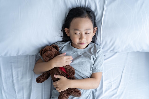 Bovenaanzicht kind klein Aziatisch meisje slaapt in het bed met een speelgoedteddybeer