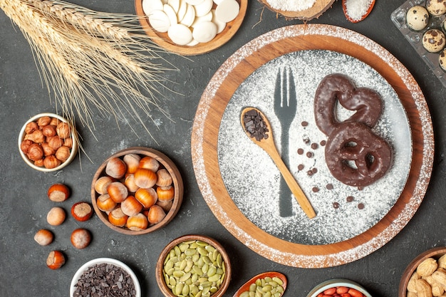 bovenaanzicht koekjes met chocolade vork opdruk met poedersuiker houten lepel op bord witte chocolade rondjes noten in kommen kwarteleitjes in gamba op tafel