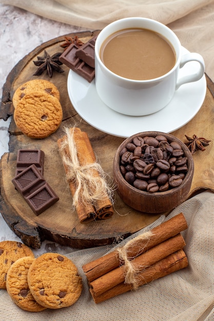 Bovenaanzicht kopje koffie koekjes kom met geroosterde koffiebonen chocolade kaneelstokjes vastgebonden met touw anijs op houten bord op tafel