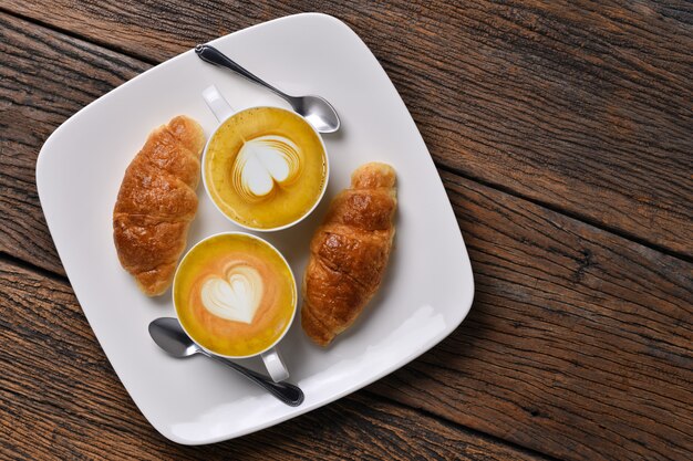 Bovenaanzicht kopje koffie latte en croissant op oude houten tafel