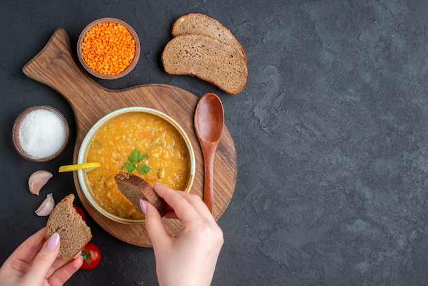 Bovenaanzicht linzensoep met vrouw die het gaat eten met donker brood op een donkere ondergrond