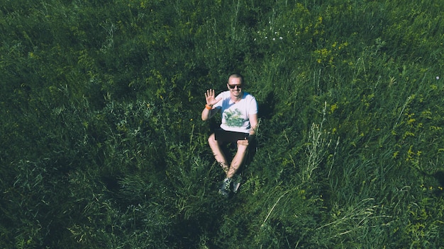 Bovenaanzicht luchtfoto van freelancer man op het gras met laptop en kijken in de camera