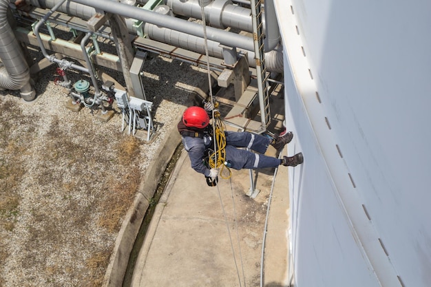 Bovenaanzicht mannelijke werknemer touwtoegang inspectie van dikte opslagtank industrie onder pijpleiding olie