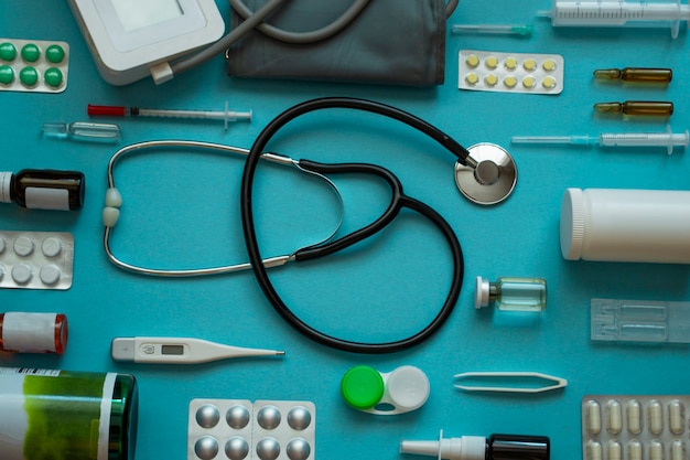Bovenaanzicht medische platte lay-out: stethoscoop, thermometer, spuit, pillen, spray, lenzen op blauwe achtergrond - bovenaanzicht platte mockup