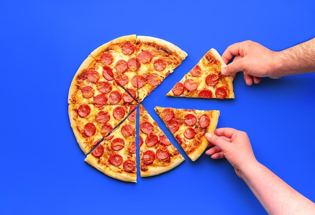 Bovenaanzicht met een gesneden pepperoni-pizza en twee handen die plakjes pizza grijpen