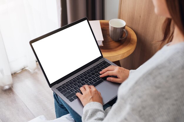 Bovenaanzicht mockup afbeelding van een vrouw die werkt en typt op een laptopcomputer met een leeg scherm terwijl ze thuis in bed zit