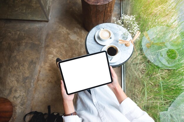 Bovenaanzicht mockup afbeelding van een vrouw met digitale tablet met leeg wit desktopscherm in café