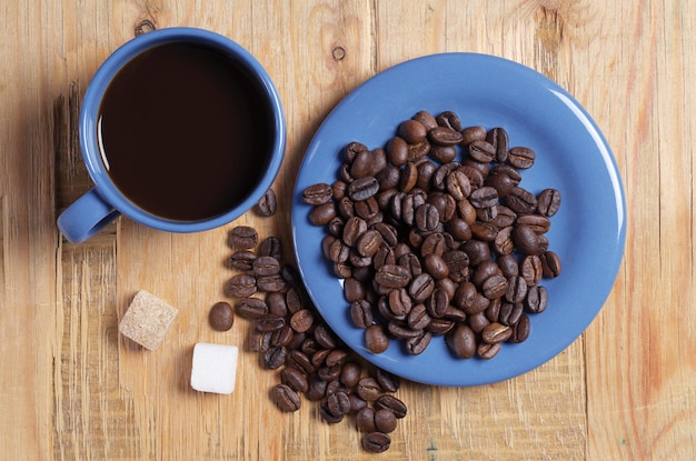 Bovenaanzicht op blauwe kop koffie, schotels met bonen en suikerklontjes op oude houten achtergrond