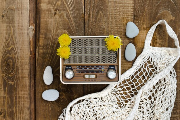 Bovenaanzicht op een houten tafel waarop een oude radio in gele paardebloemen en een boodschappentas ligt