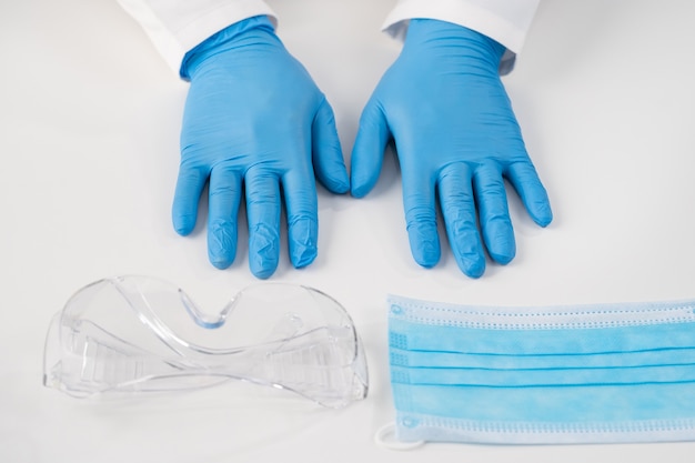 Bovenaanzicht op een wit oppervlak steriele blauwe handschoenen voor onderzoeken van plastic brillen van patiënten en een beschermend masker tegen ziektenmedische inhoud voor ziekenhuizen en klinieken