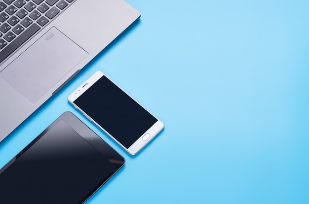 Bovenaanzicht op gadgets op blauwe achtergrond, de samenstelling van een laptop, witte koptelefoon, telefoon, glas met een drankje en autosleutels