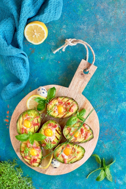 Bovenaanzicht op gegrilde avocado boten met spek en ei, plat op turkooizen achtergrond