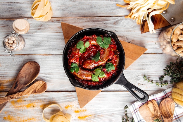 Bovenaanzicht op gekookte grote worst in tomatensaus in gietijzeren pan