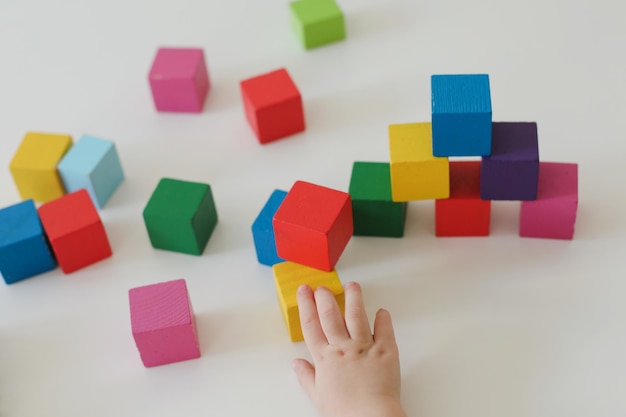 Bovenaanzicht op kinderhanden die spelen en bouwen met kleurrijke houten speelgoedbakstenen op witte houten tafel