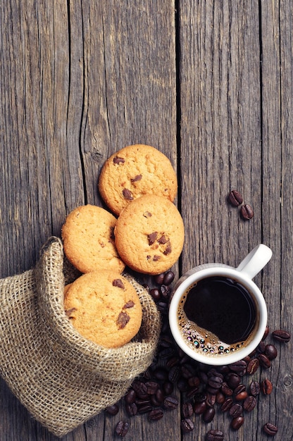 Bovenaanzicht op kopje koffie en koekjes in zak op vintage houten tafel