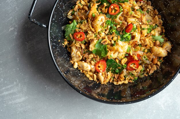 Bovenaanzicht op Pad thai, of phad thai roergebakken rijstnoedel met groenten en kip, hete chili peper en peterselie in zwarte kom op grijze stenen oppervlak