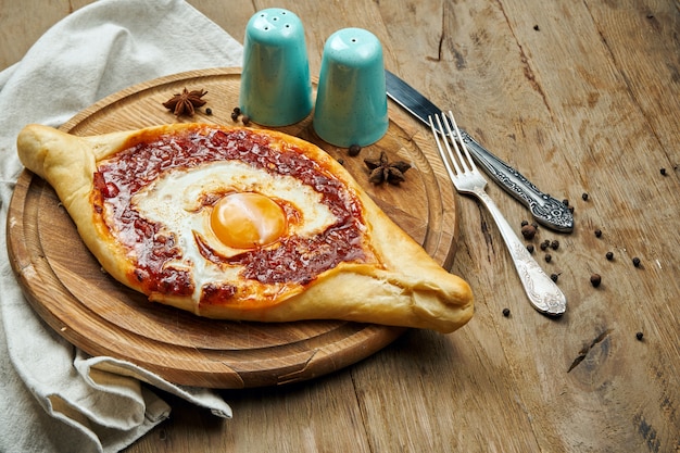 Bovenaanzicht op smakelijke traditionele Adjarian Khachapuri - open gebakken taart met gesmolten zout kaas (suluguni), tomaat en eigeel op houten dienblad. Traditioneel Georgisch eten