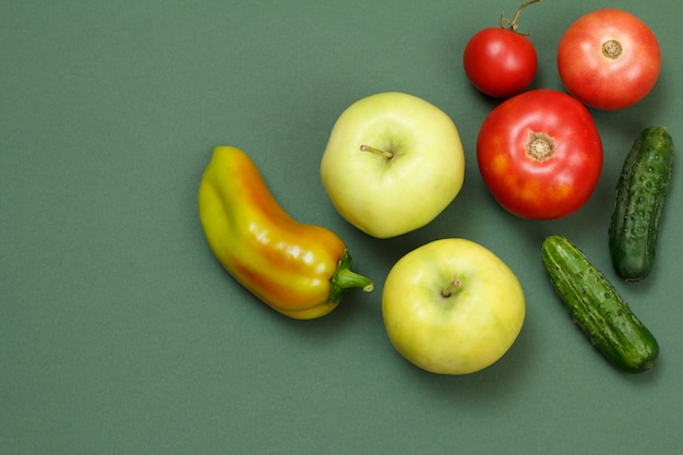 Bovenaanzicht op verse appels, paprika, tomaten en komkommers op groene achtergrond. groenten en fruit op de keukentafel.