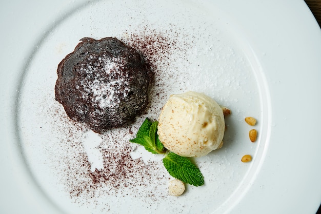 Bovenaanzicht op verse en smakelijke fondant met warme chocolademelk en ijs op witte plaat. Lekker dessert. Recept voor lavacake.