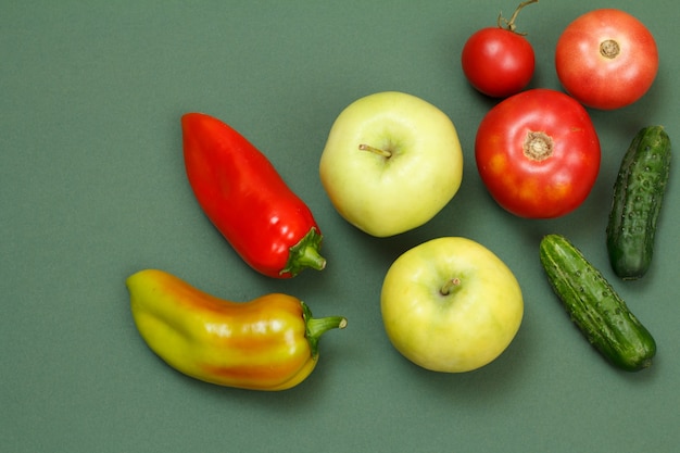Bovenaanzicht op verse paprika, appels, tomaten en komkommers op groene achtergrond. Groenten en fruit op de keukentafel.