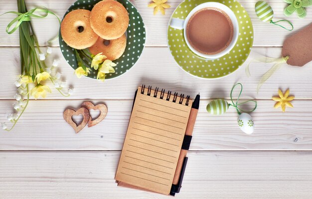 Bovenaanzicht op witte houten tafel met espresso kopje, plaat van koekjes, paaseieren en Lentebloemen