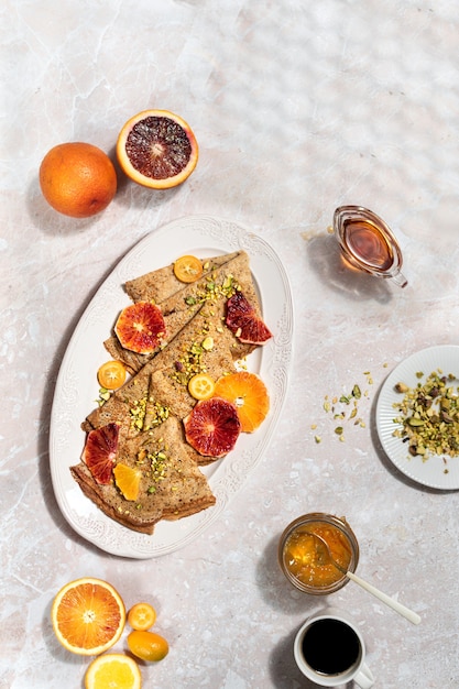 Foto bovenaanzicht pannenkoeken met bloedsinaasappelen, honing en jam op marmeren tafel, zoet ontbijt, harde schaduwen