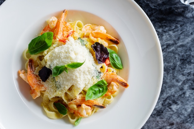 Bovenaanzicht pasta met zeevruchten, garnalen, basilicum en Parmezaanse kaas op marmeren tafel. Spaghetti in een witte kom. Traditionele Italiaanse keuken.