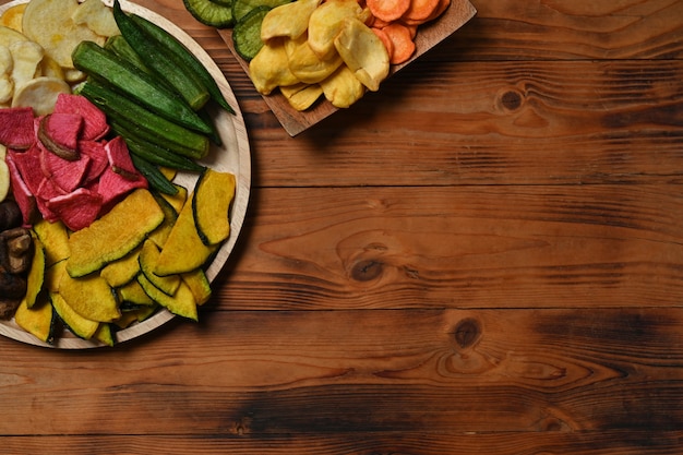 Bovenaanzicht plantaardige chips met okra, wortelen, pompoen, rode biet en shiitake-paddenstoelen op houten achtergrond.