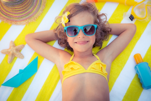 bovenaanzicht portret van meisje dat een blauwe zonnebril draagt en op een gestreept strandlaken ligt
